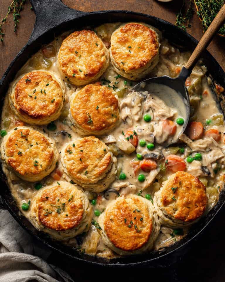 Creamy chicken pot pie dumplings in cast iron skillet with vegetables and herbs.