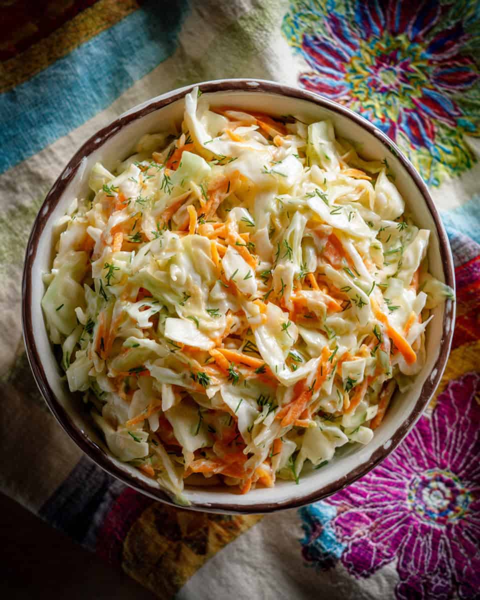 Creamy coleslaw with shredded cabbage and carrots garnished with herbs.