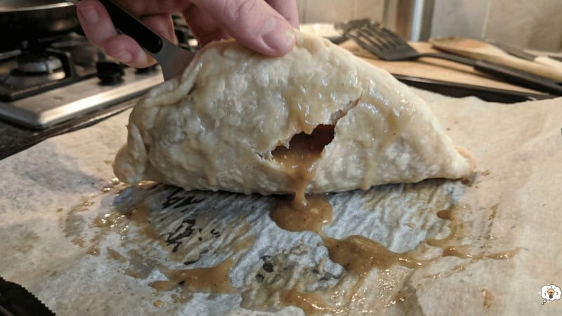 Close-up of a small Cornish pasty being held, showing the leak-proof filling inside.